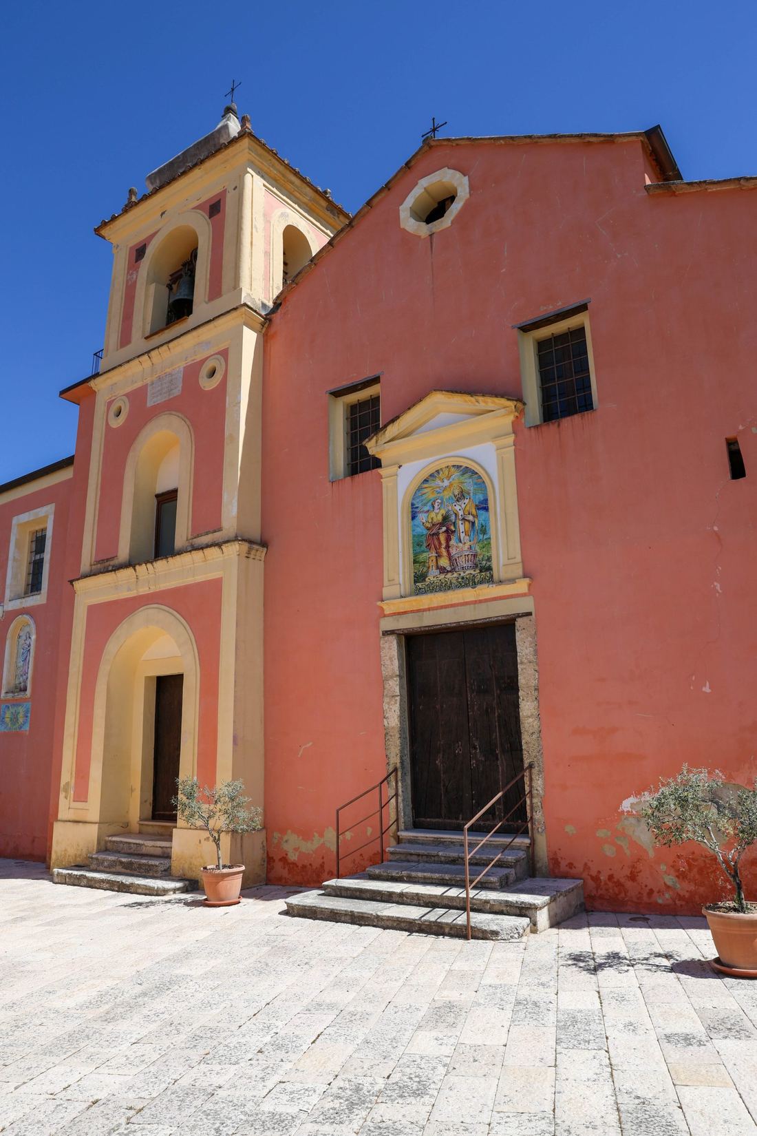 La facciata color corallo della chiesa del borgo, con il pannello di maiolica sopra il portale.