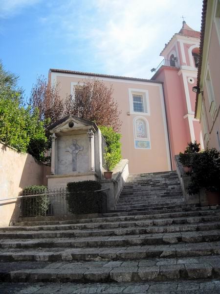 La scalinata che sale verso la chiesa, con un’edicola con la croce sulla sinistra.
