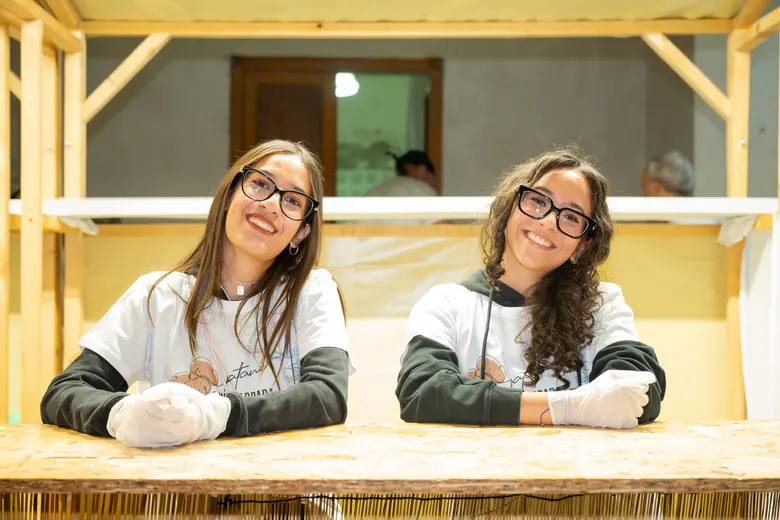 Due volontarie sorridenti dietro il bancone di legno.